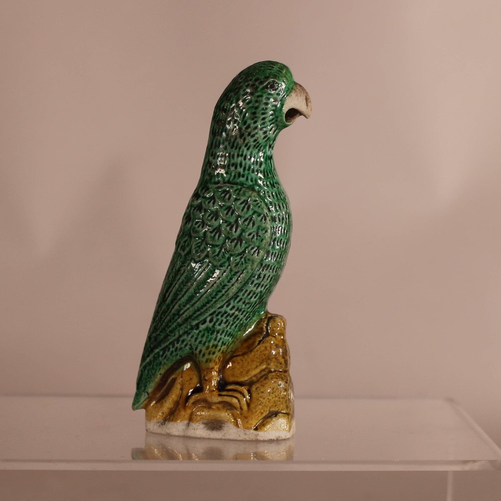 W886 A Chinese famille verte biscuit parrot,  Kangxi (1662-1722), the bird painted  with green enamel and modelled  standing on yellow rockwork,